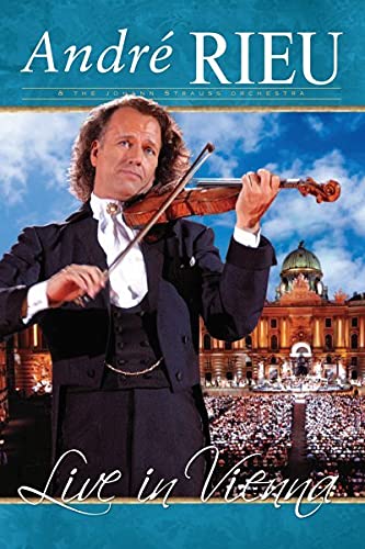 André Rieu playing violin, with a concert crowd and Vienna palace backdrop.