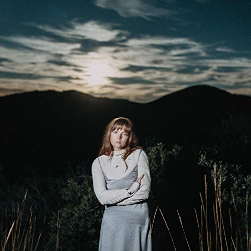 Woman in a long, light grey dress stands in a field at dusk.
