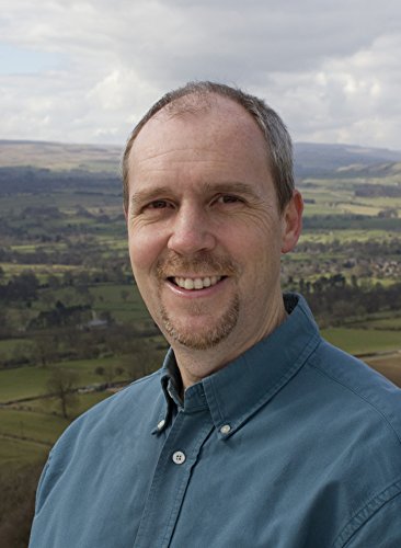 Smiling man with short hair stands before a rolling green landscape.