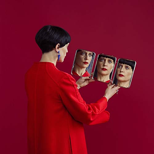 Woman in red holds three mirrors reflecting her face, red background.