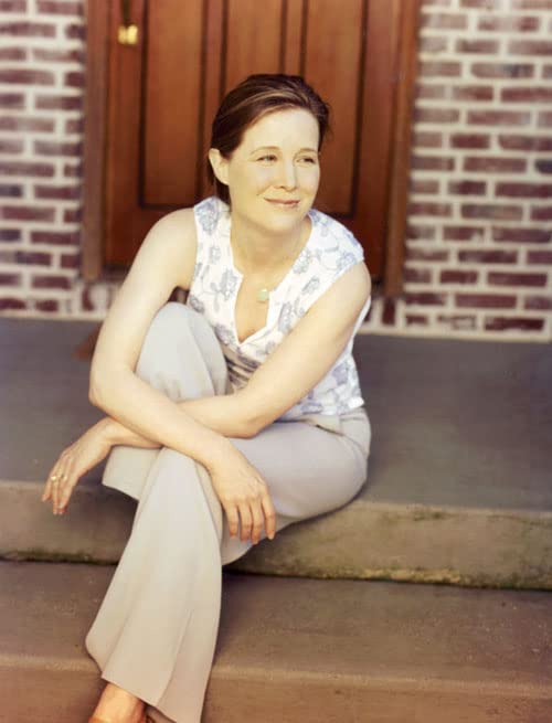 Woman with brown hair sitting on steps in front of a brick house.