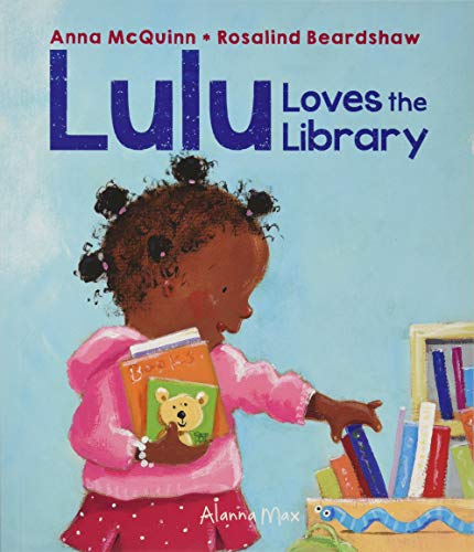A young girl with dark hair in pigtails holds books in front of library shelves.