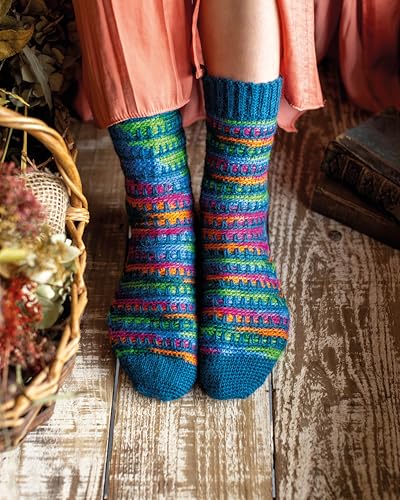 A person wears colorful, striped crochet socks while sitting on a wooden floor.