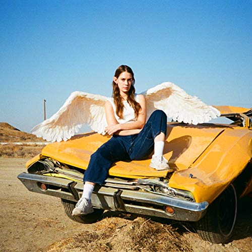 Woman with angel wings sits on a yellow, damaged car.