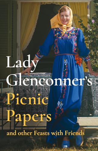 A woman in a blue embroidered dress and yellow headscarf stands outdoors near furniture.