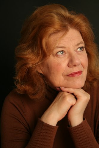 A woman with auburn hair rests her chin on her hands against black background.