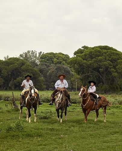 Three gauchos on horseback ride across a grassy field in Argentina.