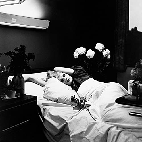 Black and white photo of a person reclining in bed with flowers.