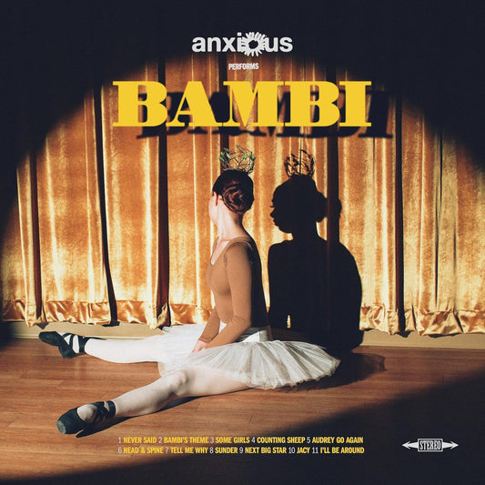 A ballet dancer with a crown sits before gold curtains under a spotlight.