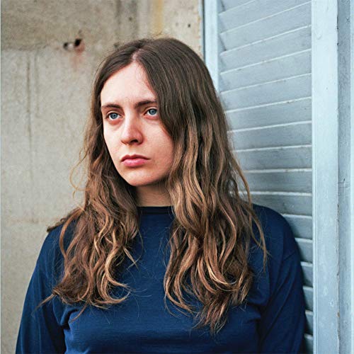 Woman with long wavy hair leaning against a shuttered wall.