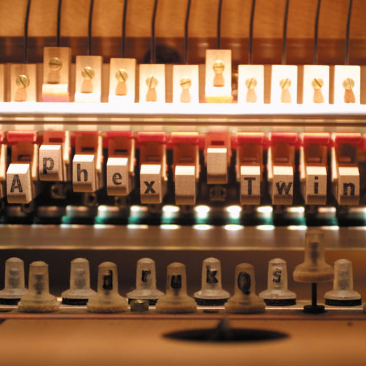 Close-up of a vintage letterpress displaying the album title "Aphex Twin Drukqs".