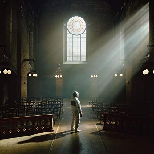 A person in a space suit stands in the aisle of a dim church.