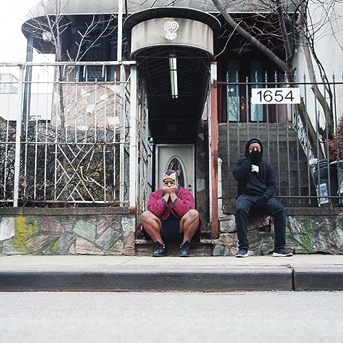 Two hooded figures sit on stone steps in front of a house.