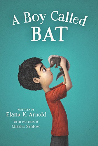 A boy in a red shirt holds a baby skunk up to his nose.