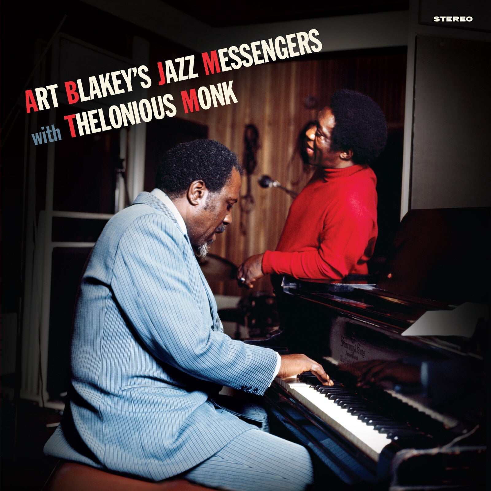 Thelonious Monk plays piano while Art Blakey stands nearby in a recording studio.