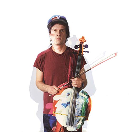 Arthur Russell with cello, wearing a cap and maroon shirt.
