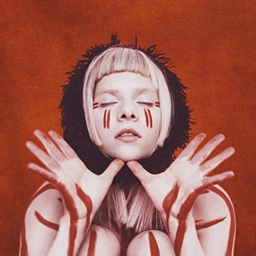 Aurora with blonde hair and red face paint, hands raised against a red background.