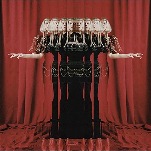A mirrored, kaleidoscopic image of a blonde woman standing before a red curtain.