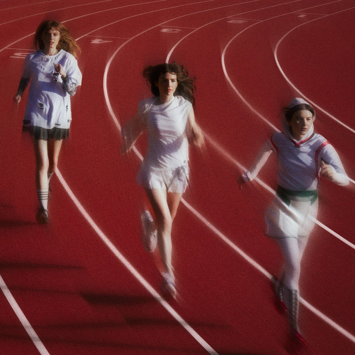 Three blurred figures in white sportswear running on a red track.
