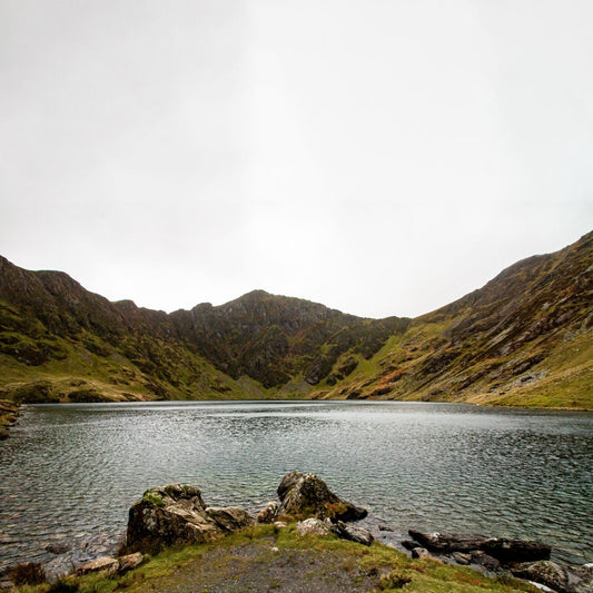 Lake surrounded by rocky, grassy mountains under a cloudy sky.