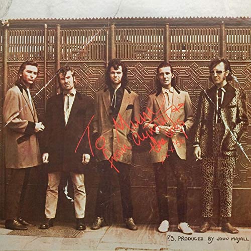 Five musicians in suits stand before an ornate metal gate.