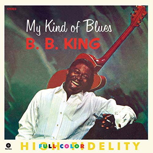 B.B. King smiling in a white shirt with a guitar on a green background.