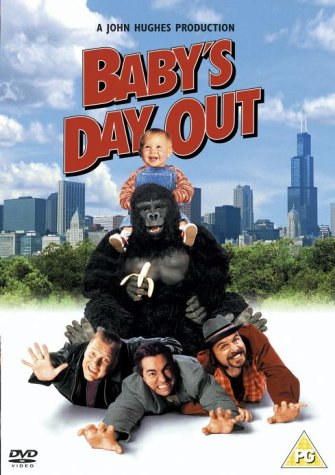 A baby sits on a gorilla's shoulders with three men lying on the ground below.