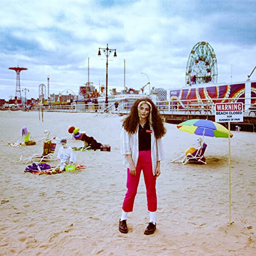 A person stands on a beach with skeletons in chairs near a closed sign.
