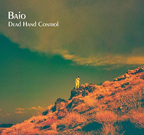 "Album cover with a person standing on a rocky hill under a cloudy sky."