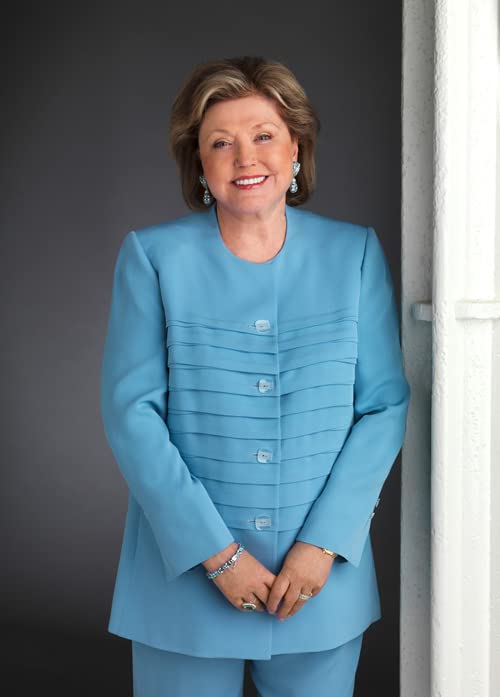 Portrait of a smiling woman with blonde hair wearing a blue pleated suit.