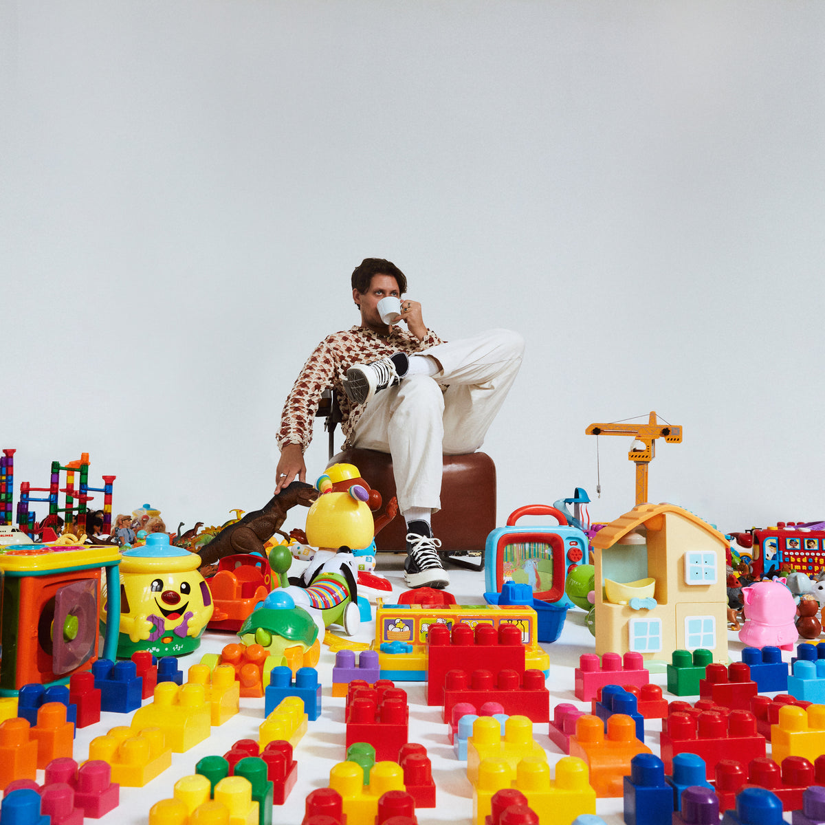 Man with a mug seated amongst colorful plastic building blocks and toys.