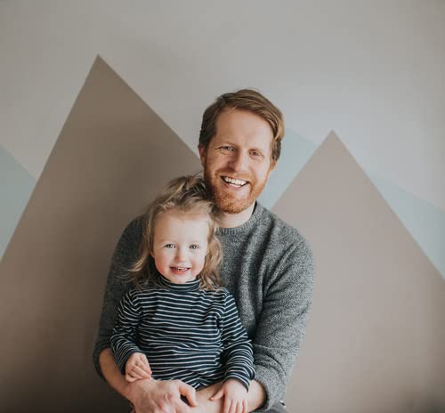 Man holding a smiling toddler in front of a geometric wall.