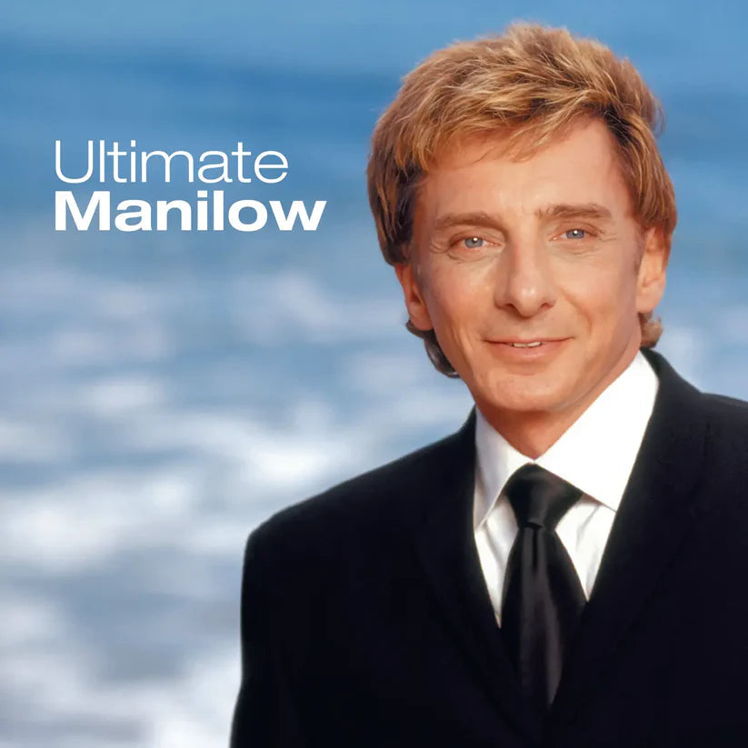 Barry Manilow in a black suit and tie against a blurred ocean background.