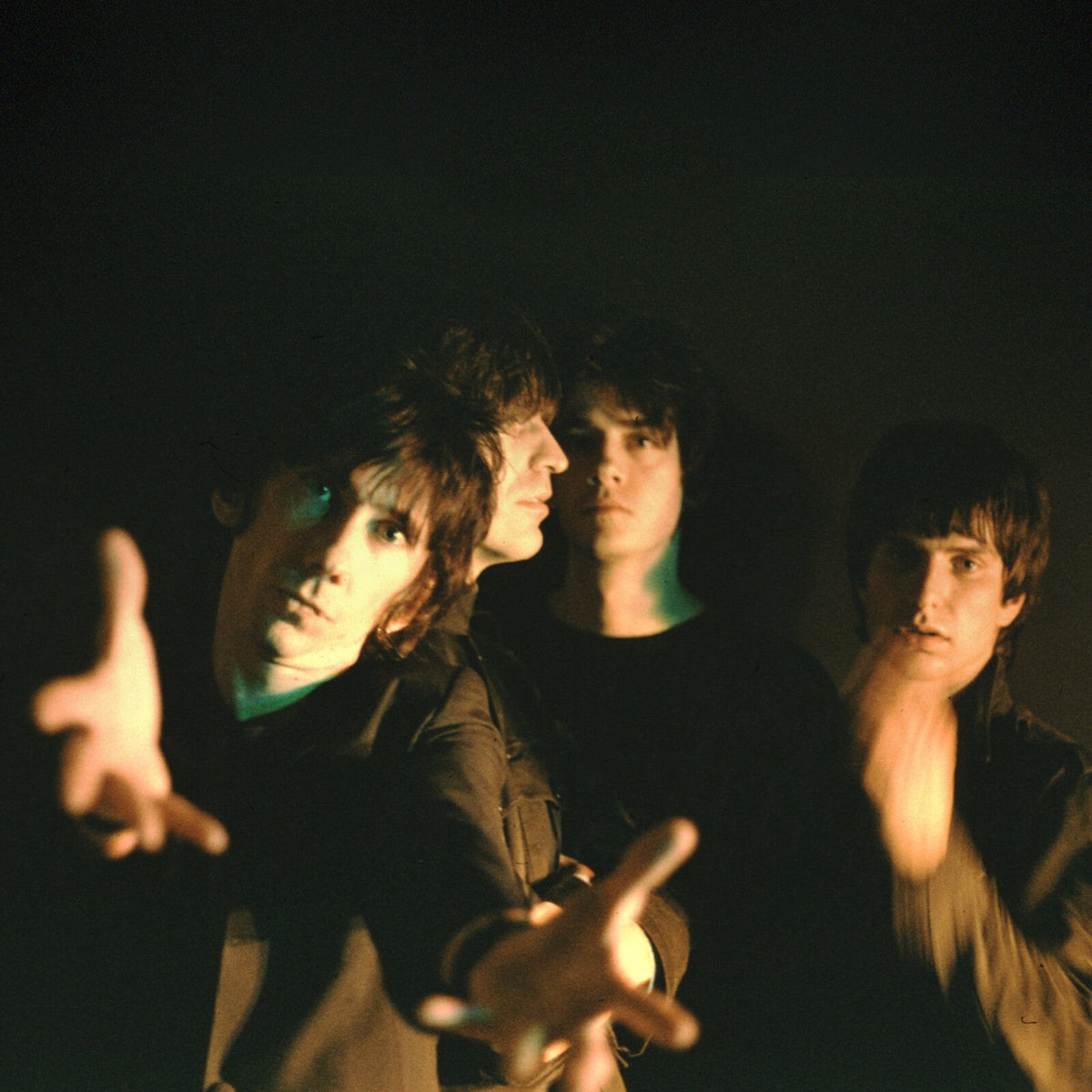 Four young men with dark hair in a dimly lit, grainy portrait.