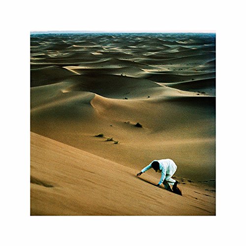 Man in white crawls down a sand dune in a desert landscape.