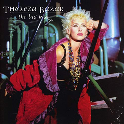 Thereza Bazar with short blonde hair wearing a red jacket and beaded necklace.