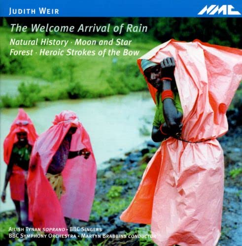 Three people in pink raincoats walking near a river, with lush greenery in background.