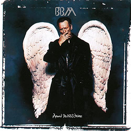 Man in a black coat with large white angel wings against a dark background.