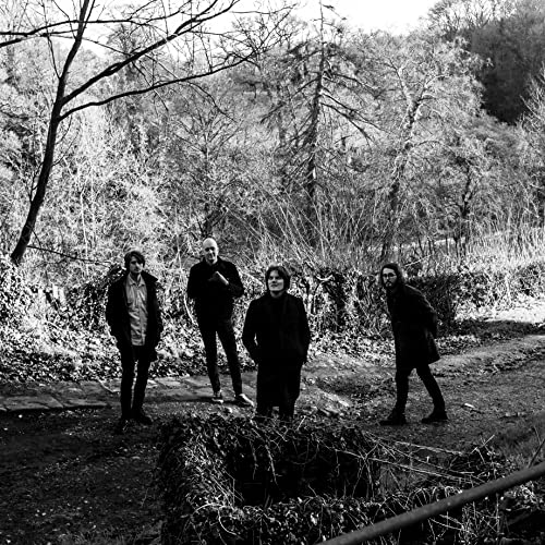 Black and white photo of four people standing in a wooded area.