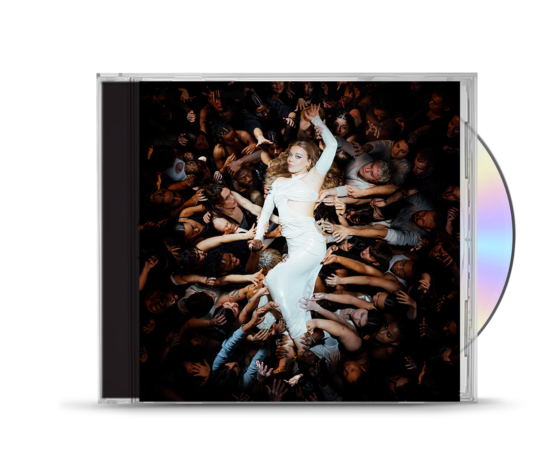 Becky Hill in a white dress surrounded by many hands in a dark crowd.
