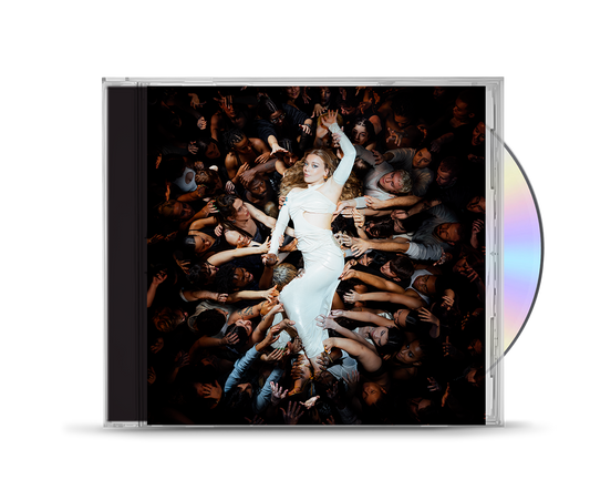 Becky Hill in a white dress surrounded by many hands in a dark crowd.