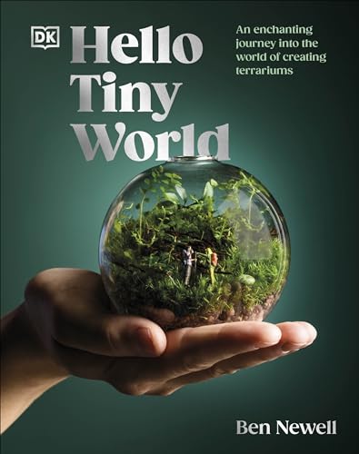 A hand holds a glass terrarium containing miniature figures and lush green plants.