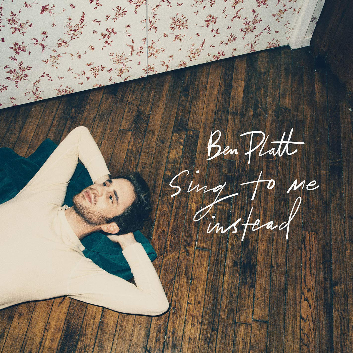 Ben Platt lying on a wooden floor against a floral wallpaper, album cover artwork.