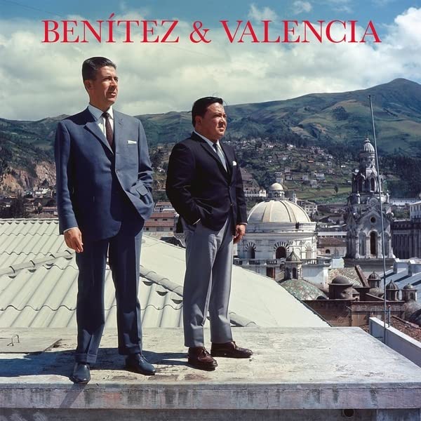 Two men in suits stand on a rooftop overlooking Quito, Ecuador.