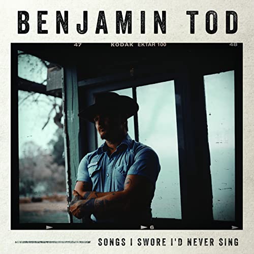 Benjamin Tod wearing a cowboy hat and blue shirt, posed in a window frame.