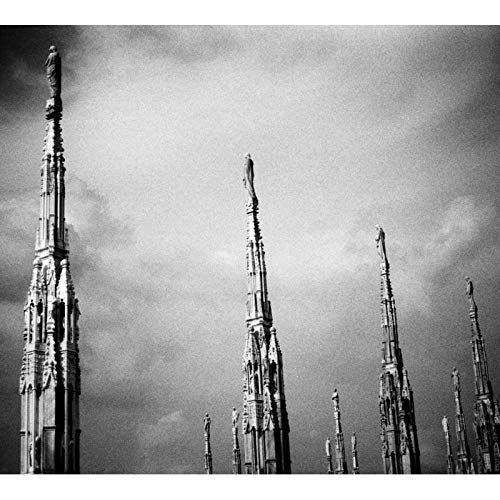A black and white image of Gothic cathedral spires against a cloudy sky.