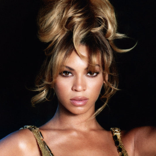 Beyoncé with voluminous blonde hair, facing forward against a dark background.