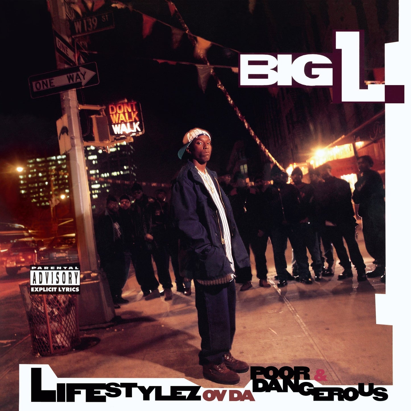 Big L stands on a city street at night surrounded by a group of men.