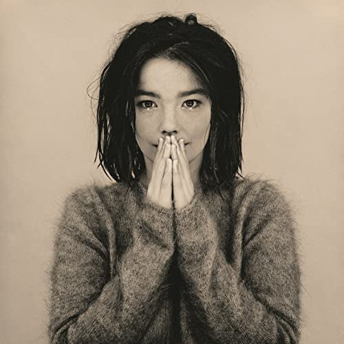 Sepia-toned portrait of Bjork with dark hair, wearing a fuzzy sweater, hands near face.