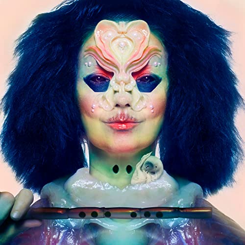 Björk with elaborate facial prosthetics, dark hair, and a flute against a pale background.